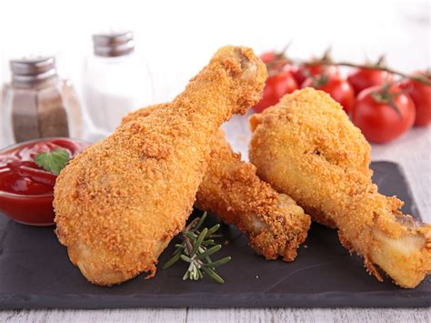 Two fried chicken legs on a plate with tomatoes and ketchup