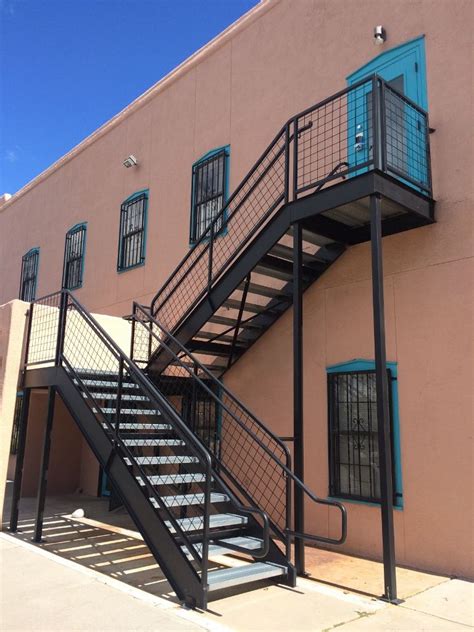 A Metal Stair Case Next To A Pink Building With Blue Shutters And