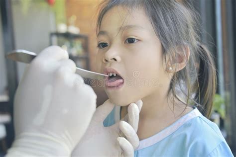 Asian Doctor In Surgical Gown Examining A Little Cute Asian Patient Girl With Throat Sick In