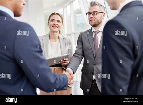 Confident Employee Greeting Business Partner With Co Workers Near By