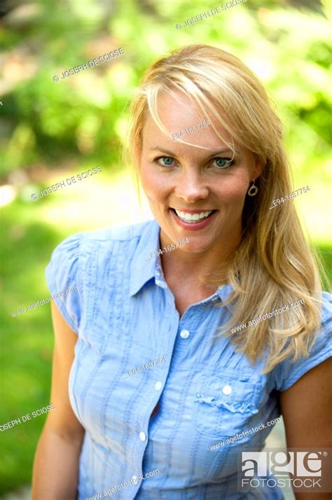 portrait of a 35 year old blond woman wearing a blue blouse and jeans in a garden setting
