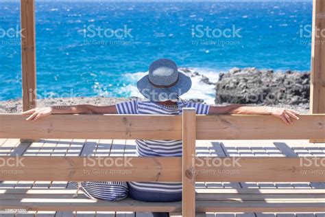 Rear View Of Mature Woman Dressed In Blue Admiring The Sea Looking At