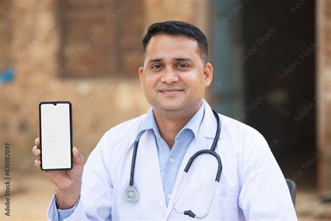 Young Positive Indian Male Doctor Wearing Stethoscope Showing Smart Phone With Blank Display