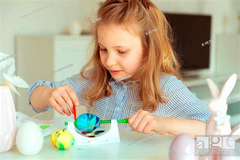 Cute Little Blonde Girl Painting Easter Eggs At Home Stock Photo