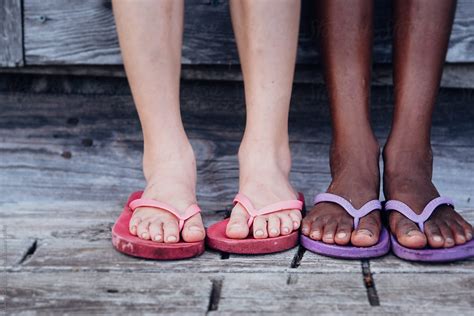 caucasian and african american girl s legs with flip flops outside a wooden shack by stocksy