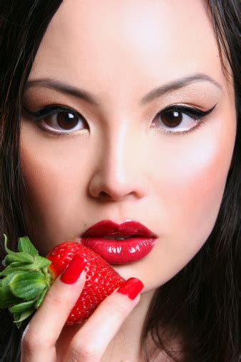 Asian Woman Holding Strawberry To Glossy Red Lips Stock Photo