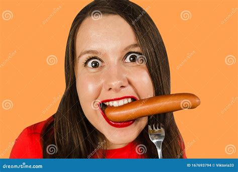Joven Linda Comiendo Salchicha En Un Tenedor En Su Boca En Un Fondo Naranja Foto De Archivo