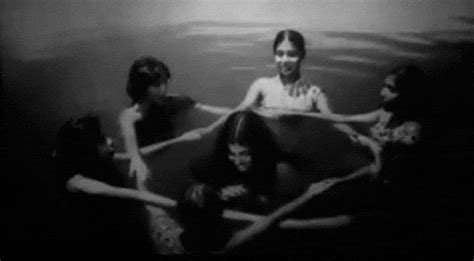 Black And White Photograph Of Four People Sitting In The Water With Their Arms Around Each Other