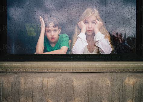 Children Looking Out A Window On A Rainy Day By Stocksy Contributor