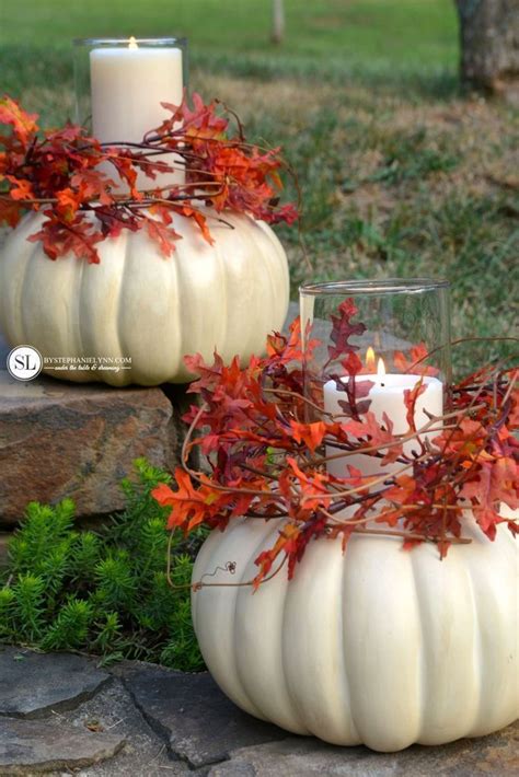 Two White Pumpkins With Candles In Them Sitting On Some Rocks And Grass