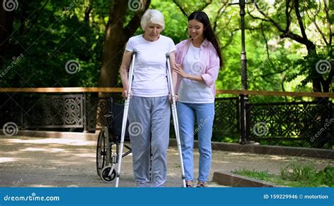 Female Volunteer Helping Disabled Senior Woman Walk With Frame In Park