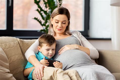 Madre E Hijo Embarazadas Con Smartphone En Casa Foto De Archivo