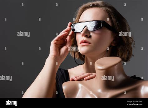 Overweight Young Woman Adjusting Sunglasses And Posing With Plastic Mannequin Isolated On Grey