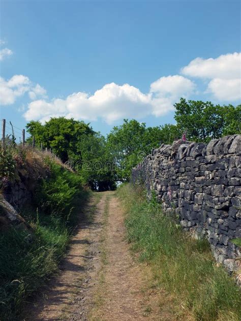 Narrow Country Lane Running Up A Hill Surrounded By Stone Walls And