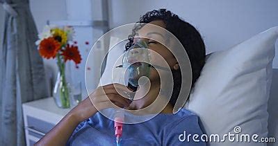 Portrait Of African American Female Patient Lying On Hospital Bed Wearing Oxygen Mask Ventilator