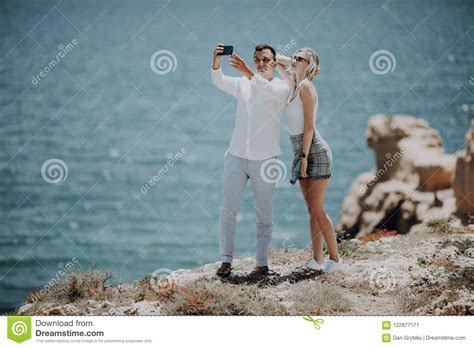Young Couple Taking Selfie Self Portrait Photo On The Top Of Cliff On Ocean Background Happy