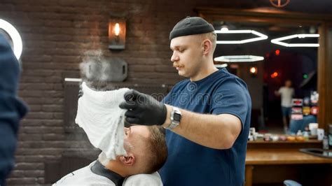 traditional ritual of shaving side view of male barber with a mustache covering face of client