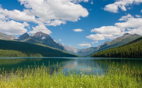 Fluffy White Clouds In The Blue Sky Above The Mountain Lake Wallpaper