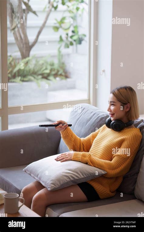 Mujer joven que ve la televisión que descansa en el sofá que se sienta en la sala de estar en