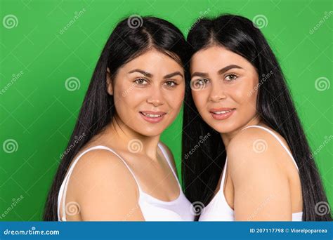 portrait of cute twins brunettes on a green background posing and smiling looking at the camera