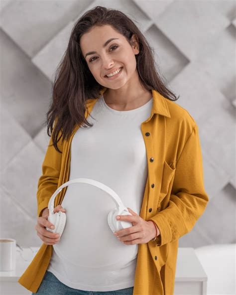 Mujer Embarazada Sonriente Sosteniendo Auriculares En Su Vientre Foto