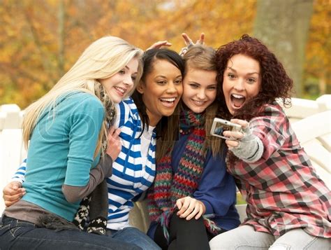 Group Of Four Teenage Girls Taking Picture With Camera Sitting On Bench