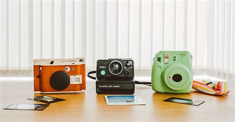 Three Assorted Color Instant Cameras On The Table With Sample Photos