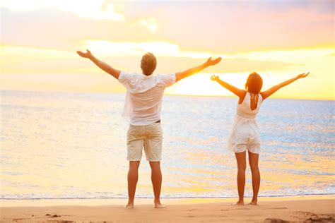 Happy Cheering Couple Enjoying Sunset At Beach With Arms Raised Men