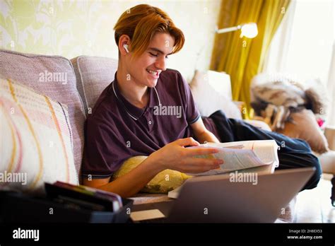 Smiling Teenage Boy With Textbook And Laptop Studying At Home Stock