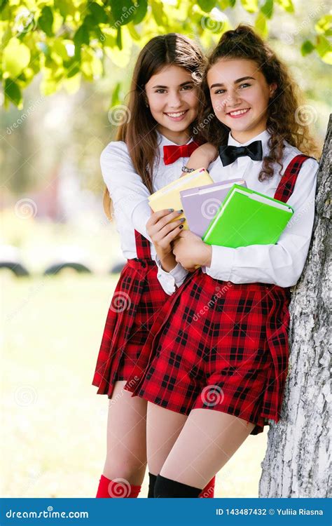 dos colegialas bonitas en soporte del uniforme escolar con los libros al aire libre en el parque