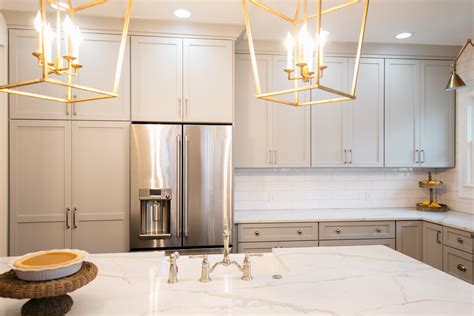 A Kitchen With White Marble Counter Tops And Gold Chandelier Hanging