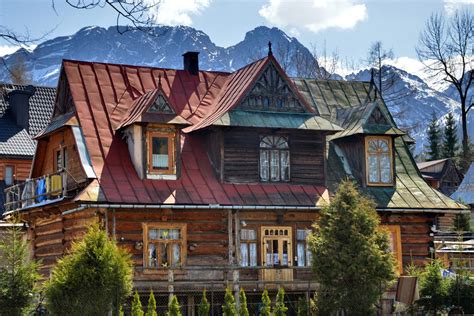 An Old Wooden House With Red Roof Tiles And Mountains In The Backgrouds