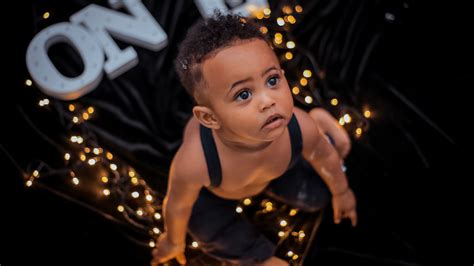 Cute Baby Boy Is Sitting On Floor With Lights Looking Up
