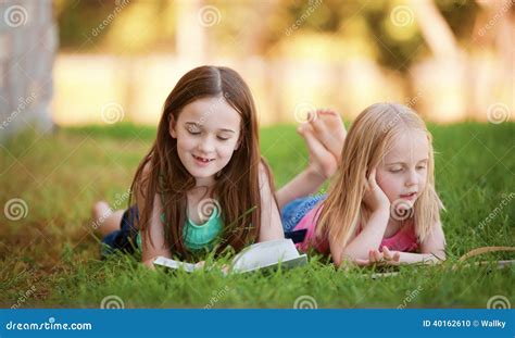 Twee Jonge Meisjes Die Op Het Gras Liggen Die In Openlucht Een Boek Lezen Stock Foto Image Of