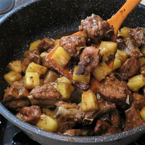 A Skillet With Meat And Potatoes Cooking On Top Of The Stovetop Next To