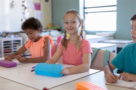 Schoolgirl With Blonde Plaits Sitting At A Desk In An Elementary School Classroom Stock Image