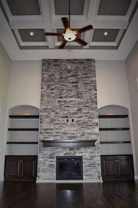 A modern farmhouse fireplace complemented with a wooden mantle, hardwood flooring, and our european styled stone veneer. 2 Story Great Room, Coffered Ceiling, Stone Fireplace ...