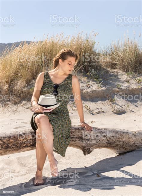 A Middleaged Blonde Woman Sitting On A Tree Trunk At The Beach Stock