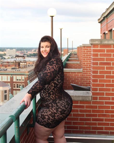 A Woman Posing On Top Of A Building Next To A Brick Wall And Green Railing