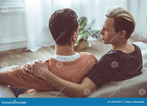Gay Couple Cuddling And Looking At Each Other While Sitting On Couch Stock Image Image Of