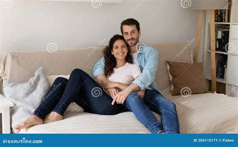 Portrait Of Young Wife And Husband Hugging Sitting On Cozy Couch Stock