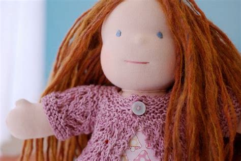 A Doll With Long Red Hair Wearing A Pink Shirt And Holding Her Hands