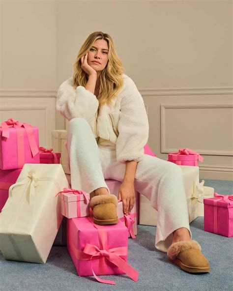 A Model In Ugg Shoes And Loungewear Sitting On A Pile Of Brightly Colored Wrapped Presents