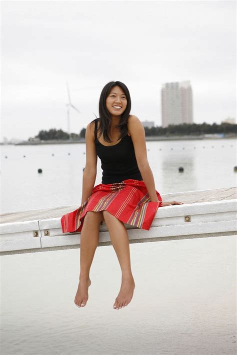 A Woman Is Sitting On A Ledge By The Water Smiling At The Camera While Wearing A Red Skirt And