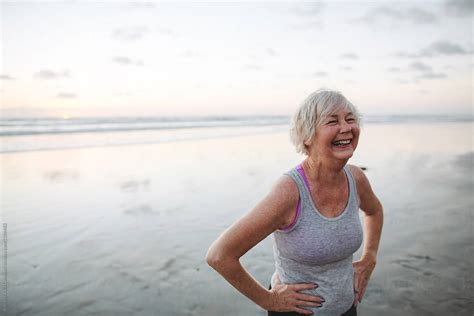 vibrant mature woman enjoying herself on the beach at sunset by stocksy contributor rob and