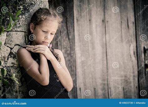 Portrait Of Sad Little Girl Standing Near Stone Wall In The Day Stock