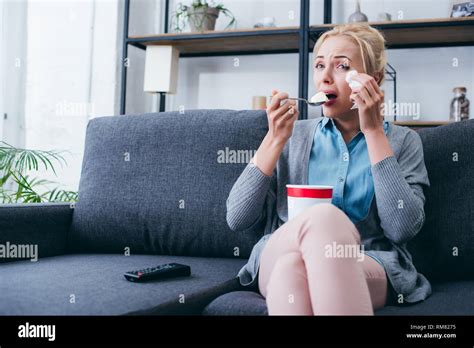 Woman Eating Ice Cream And Crying While Siitng On Couch And Watching Tv At Home Alone Stock