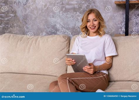 Blonde Woman Sitting On Couch Using Tablet At Home In The Living Room Stock Photo Image Of