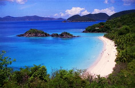 A Beach With Blue Water Surrounded By Green Trees And Mountains In The