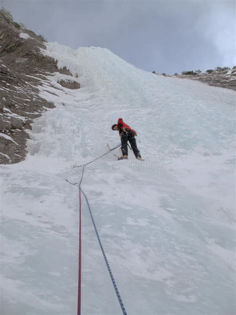 Male Mountain Ice Climber Climbing A Steep And Long Frozen Waterfall In